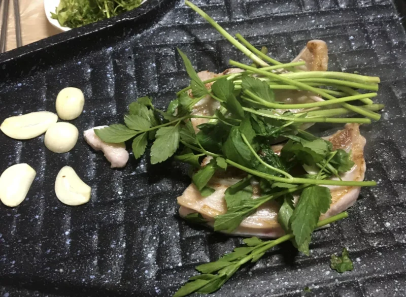 [불판 위에서 삼겹살과 푸릇푸릇한 미나리가 함께 구워지는 먹음직스러운 사진] 출처: https://tour.gb.go.kr/tip/storyView.do?idx=17220